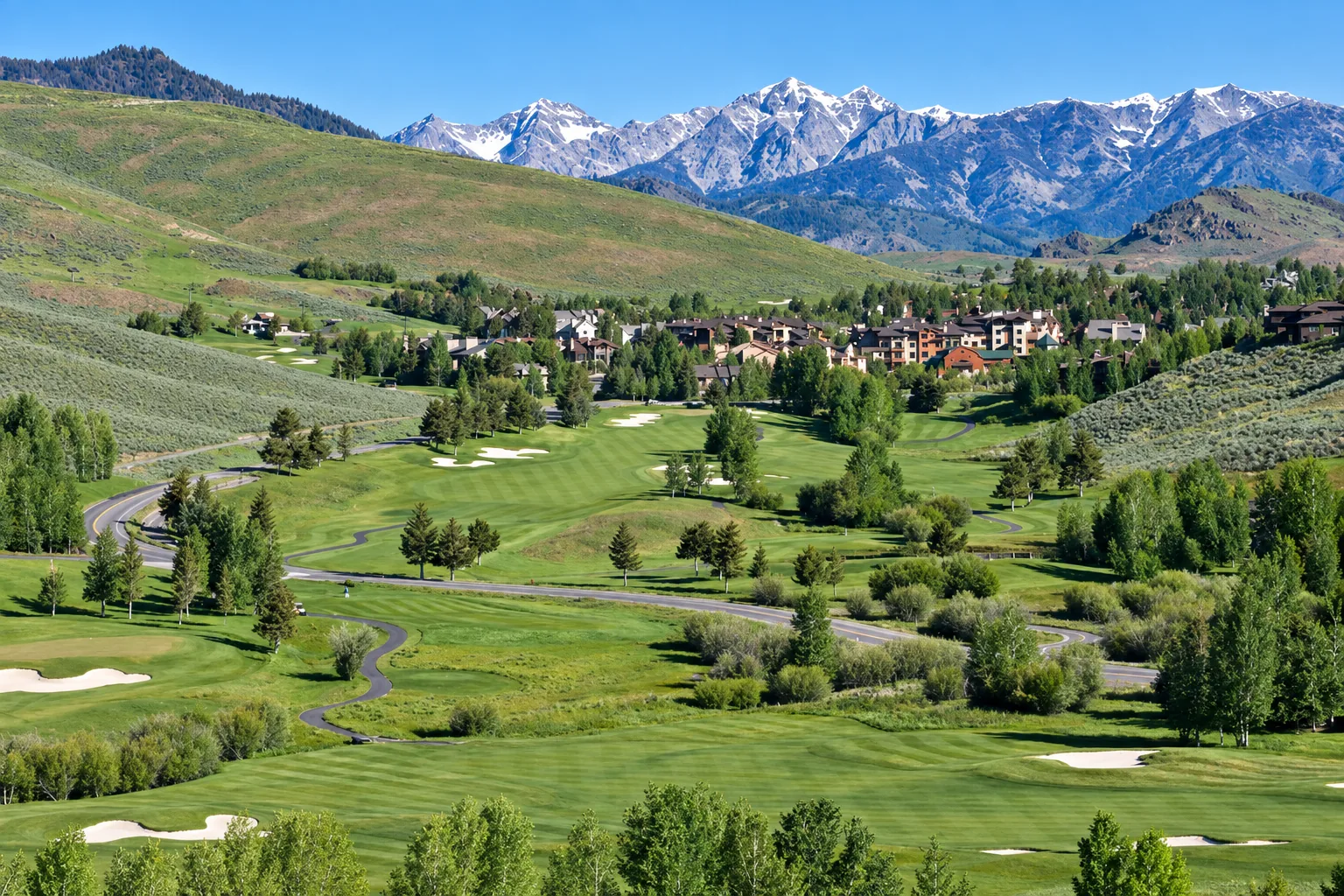 Elkhorn golf course and homes among green hills, with snow-streaked mountain peaks beyond.