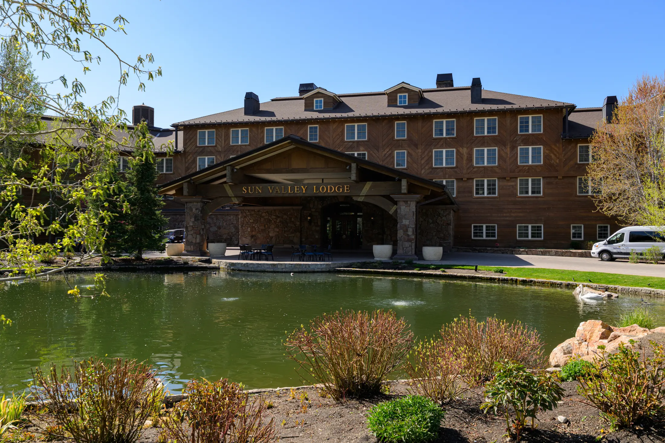 Sun Valley Lodge overlooking its pond, framed by trees and a blue sky.